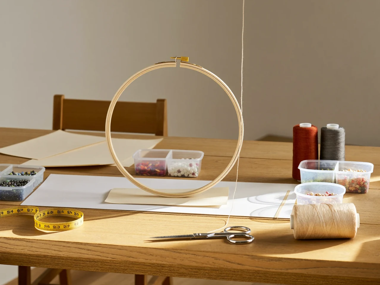 Craft table with thread, paper, beads and tools arranged around an embroidery hoop