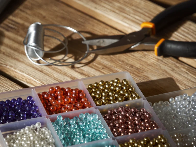 Compartment tray of glass seed beads beside fine wire and round-nose pliers